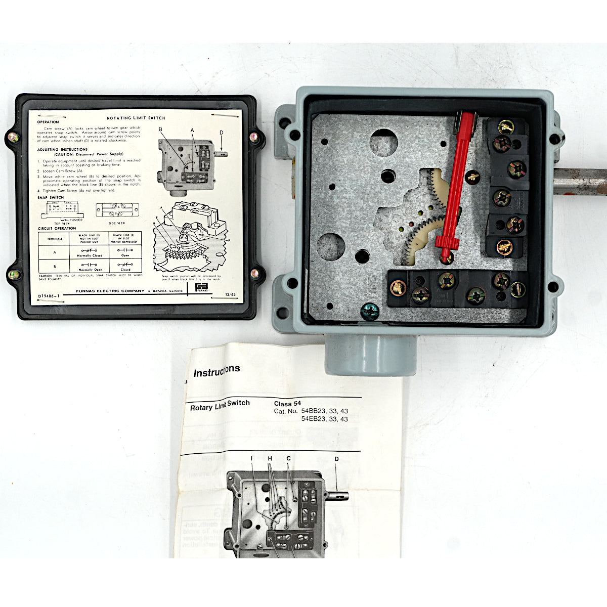 An open electrical battery switch enclosure with internal components visible, shown alongside its cover panel and printed instruction booklet on a white background.