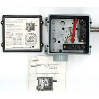 An open electrical battery switch enclosure with internal components visible, shown alongside its cover panel and printed instruction booklet on a white background.